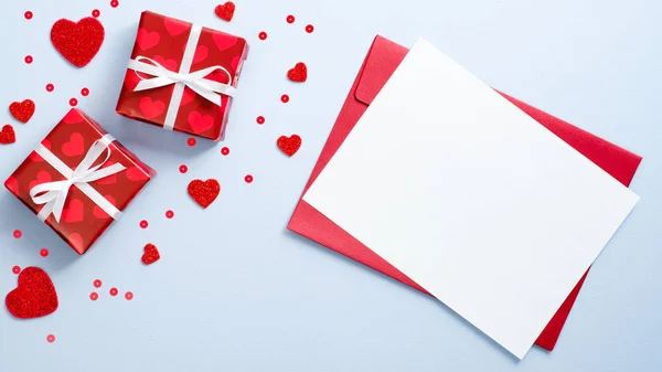 Sobre rojo con tarjeta de papel en blanco y cajas de regalo decoradas corazones sobre fondo azul. Concepto de carta romántica. Feliz día de San Valentín plana composición laica . —  Fotos de Stock
