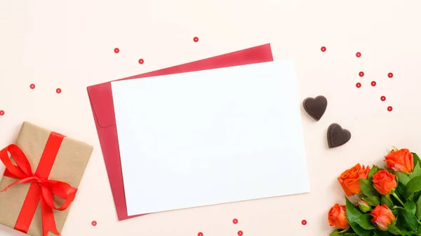 Concept de Saint-Valentin. Lettre romantique, coffret cadeau avec ruban rouge, fleurs de roses et confettis sur fond beige pastel. Pose plate, vue du dessus, espace de copie . — Photo