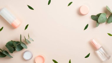 Doğal organik kozmetik şişelerden yapılmış çerçeve. Pastel bej arka planda yeşil bitkisel yapraklar var. Doğal güzellik ürünü konsepti. Güzellik blogu için afiş modeli. Düz yatış, üst görünüm.