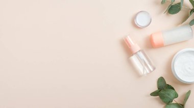 El bakımı için gerekli yağı içeren şeffaf kozmetik şişe kapları ve pastel bej arka planda yeşil bitkisel yapraklar. Doğal güzellik ürünü konsepti. En düşük düz konum biçimi.
