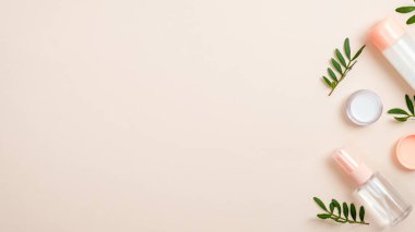 El bakımı için gerekli yağı içeren şeffaf kozmetik şişe kapları ve pastel bej arka planda yeşil bitkisel yapraklar. Doğal güzellik ürünü konsepti. En düşük düz konum biçimi.