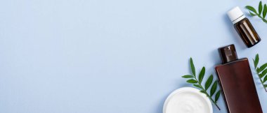 Kozmetik şişe kapları düzdü. Beyaz yüz kremli üst görüş kavanozu, saç büyümesi için biberiye yağı, pastel mavi arka planda merhem şampuanı ve biberiye yaprakları. Doğal güzellik ürünü konsepti.