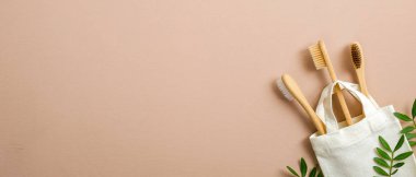 Doğal bambu diş fırçaları ve yeşil yapraklarla bez kumaş alışveriş torbası. Düz konum, üst görünüm, kopyalama alanı. Çevre mağazası web pankartı. Organik ürünler, sıfır atık, plastiksiz konsept.