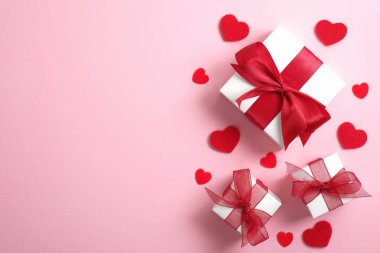 Sevgililer günün kutlu olsun. Kırmızı kurdeleli beyaz hediye kutuları ve pembe arka planda kırmızı kalpler. Düz yerde, üst tarafta, tepede. Sevgililer günü, yıldönümü, anneler günü ve doğum günü selamı.