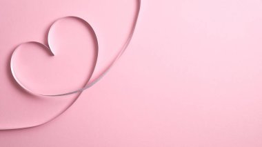 Pembe arka planda gümüş kurdeleden yapılmış kalp şeklindeki kenar. Sevgililer Günü tebrik kartı maketi, fotokopi alanı olan minimal düz konum kompozisyonu. Aşk konsepti.