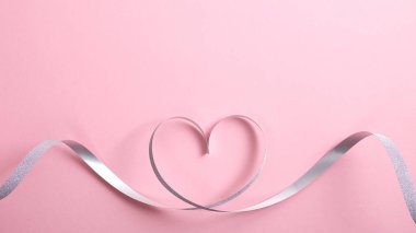 Pembe arka planda gümüş kurdeleden yapılmış kalp şeklindeki kenar. Sevgililer Günü ya da doğum günü için tebrik kartı maketi. Anneler Günü. Aşk konsepti. Düz yatış, üst görünüm.