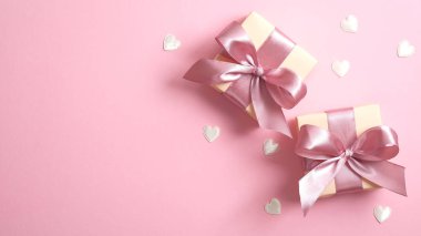 Pembe kurdeleli iki hediye kutusu ve pembe arka planda sevgililer günü kalpleri. Düz yerde, üst tarafta. Sevgililer günün kutlu olsun ya da anneler günü afişin..