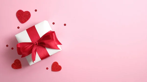 Caja de regalo de papel blanco con lazo de cinta roja sobre fondo rosa con corazones de San Valentín. Piso tendido, vista superior, espacio para copiar. Banner o tarjeta de felicitación maqueta para San Valentín o el Día de la Madre —  Fotos de Stock