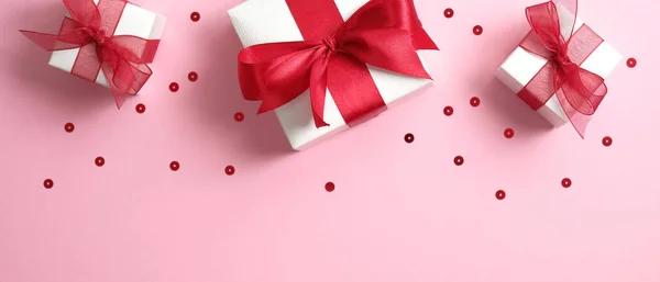 Banner del día de San Valentín con cajas de regalo blancas decoradas con lazo de cinta roja sobre fondo rosa con confeti. Piso tendido, vista superior . — Foto de Stock