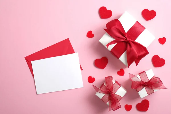 Carta de amor con nota de papel en blanco y cajas de regalo blancas con lazo de cinta roja sobre fondo rosa pastel decorado corazones rojos. Asiento plano, vista superior. Sorpresa del día de San Valentín, concepto de amor . — Foto de Stock