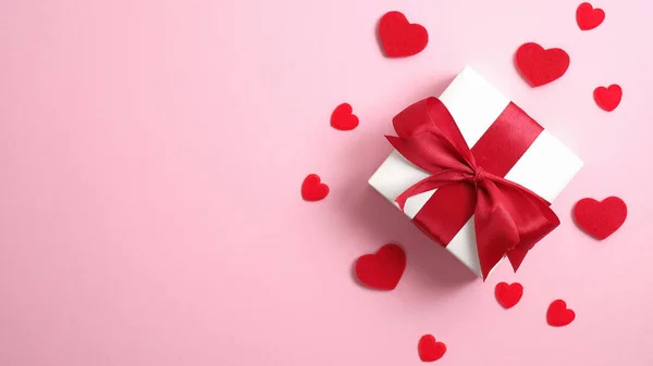Gelukkige Valentijnsdag spandoek. Witte geschenkdoos met rood lint strik en rode hartjes op roze achtergrond. Platte lay, bovenaanzicht, bovenleiding. — Stockfoto