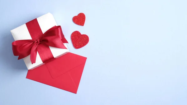 Vit presentask med rött band båge, rött papper kuvert och hjärtan på blå bakgrund. Platt ligg, ovanifrån. Banner mockup för Saint Valentines dag. Kärlek och romantik koncept — Stockfoto