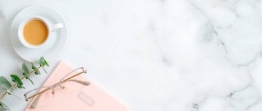 Pembe kağıt not defteri, kadın bardakları, bir fincan kahve, mermer arka plandaki okaliptüs yaprağı ve fotokopi alanı. Güzellik günlüğü pankartı