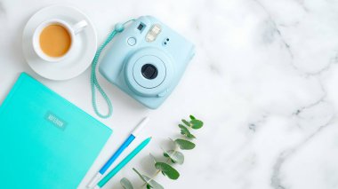 Modern fotoğraf makinesi, kahve fincanı, nane şekeri, kırtasiye malzemesi ve mermer masa üzerinde okaliptüs yaprağı olan kadınsı çalışma alanı. Düz konum, üst görünüm, kopyalama alanı. Bağımsız ofis masası konsepti.