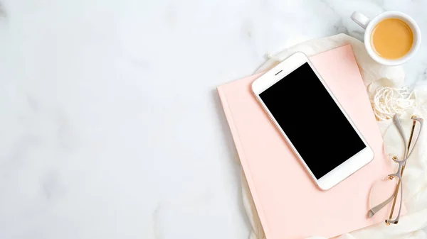 Pembe not defterli ofis masası, akıllı telefon ekran modeli, mermer arka planda kadın gözlükleri. Şık aksesuarları olan zarif kadın çalışma alanı. Düz yatış, üst görünüm.