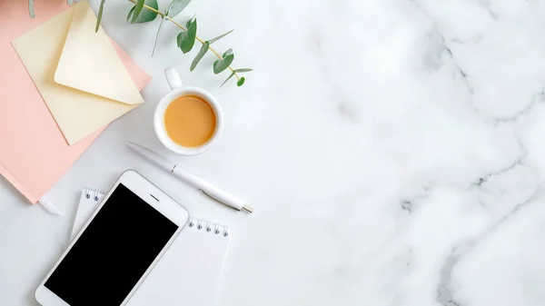 Ev ofisinin masası düzdü. Kadınlar çalışma alanında kağıt defter, kahve fincanı, zarf, bilye masanın üzerinde akıllı telefon. Kopyalama alanı olan üst görünüm kadınsı arkaplan.