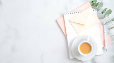 Düğün listesi, aşk mektubu, pembe not defteri, bir fincan kahve, kalem, okaliptüs yaprağı olan kadınsı çalışma alanı. Düz yerde, üst tarafta. Düğün, gelin, evlilik kavramı.