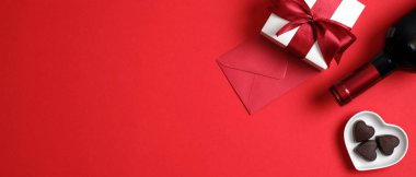 Sevgililer Günü afişleriniz kutlu olsun. Sevgililer Günü için en iyi manzara masası, bir şişe şarap şampanyası, kırmızı kurdeleli hediye kutusu, kalp şeklinde şekerler ve kırmızı arka planda fotokopi alanı olan zarf.