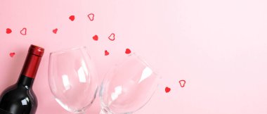 Sevgililer Günü arka planında bir şişe şarap şampanya, iki bardak ve pembe üzerine kalp şeklinde konfeti. En az düz konum biçimi, üst görünüm. Sevgililer Günü, romantik akşam yemeği konsepti.