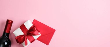 Sevgililer Günü afişi, bir şişe şarap, hediye kutusu, pembe arka planda aşk mektubu olan kırmızı zarf. Sevgililer Günü kutlama konsepti. Düz konum, üst görünüm, kopyalama alanı