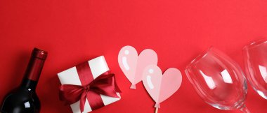 Sevgililer Günü konseptin kutlu olsun. Romantik yemek masasında şarap şişesi şampanya, bardaklar, kırmızı kurdeleli beyaz hediye kutusu, kırmızı arka planda pembe kalpler. Sevgililer Günü afiş şablonu