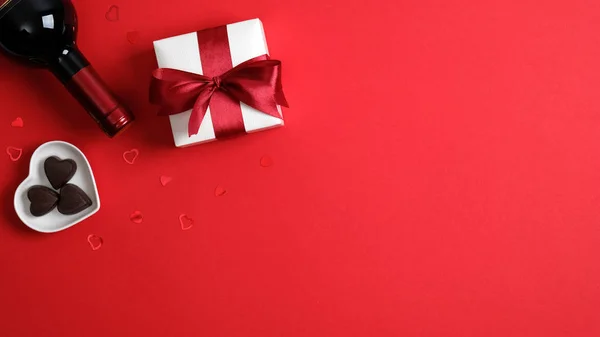 Fondo de San Valentín con botella de champán de vino, caja de regalo blanca con cinta roja, caramelos en forma de corazón en la mesa roja. Piso tendido, vista superior, espacio para copiar. banner de San Valentín maqueta, volante, cartel — Foto de Stock