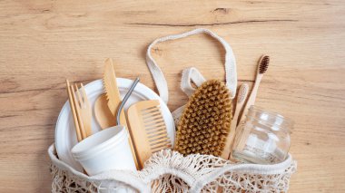 Sıfır atık. Çevre dostu mutfak eşyaları ve banyo malzemeleriyle pamuk iplik alışveriş torbası. Bambu çatal bıçak seti, tarak, spa fırçası, cam kavanoz, ahşap masada diş fırçası.