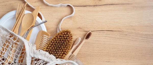 Zero waste concept. Cotton String Shopping Bag with Eco-Friendly tableware and bathroom items. Top view shopper with bamboo cutlery set, comb, spa brush, toothbrushes on wooden table. Sustainable life — Stock Photo, Image