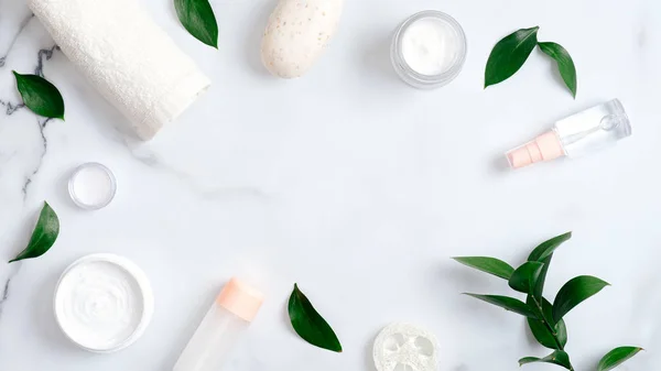 Natural cosmetic products and green leaves on marble background. Frame made of towel, handmade soap, essential oil, luffa sponge, hand cream. Flat lay, top view. Natural organic beauty product concept