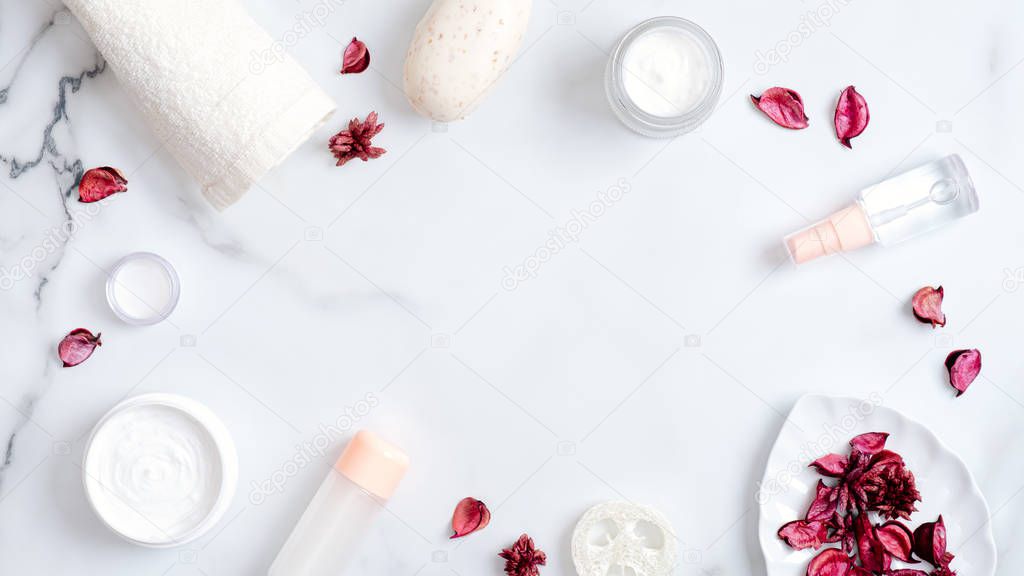 Natural cosmetic products and rose petals on marble background. Frame made of towel, handmade soap, essential oils, luffa sponge, hand cream. Flat lay, top view. Natural organic beauty product concept