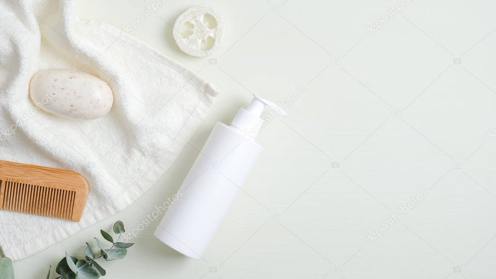 Beauty SPA cosmetic bottle container, towel, wooden hair comb, organic soap, luffa sponge, eucalyptus leaf on green background. Minimalist cosmetic product mockup, natural branding