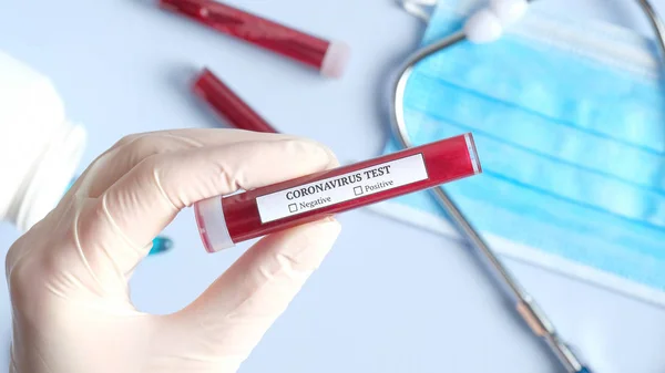 A nővér véres kémcsövet tart a Coronavirus teszthez az orvosi asztalnál légzőmaszkkal és tablettákkal. 2019-ncov vírus fertőzés származó Wuhan, Kína — Stock Fotó