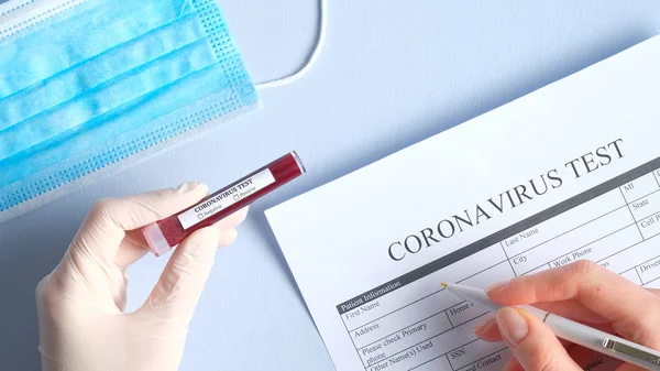 Coronavirus blood test concept. Nurse hands holding test tube with blood of patient for 2019-nCoV analysis and fills out medical form in laboratory. Chinese Wuhan virus outbreak