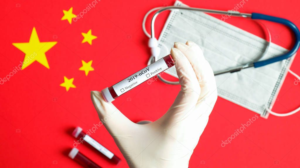 Novel coronavirus 2019-nCoV concept. Nurse hand holding blood test-tube over Chinese flag with breathing mask and stethoscope. Wuhan coronavirus outbreak, influenza pandemic virus infection