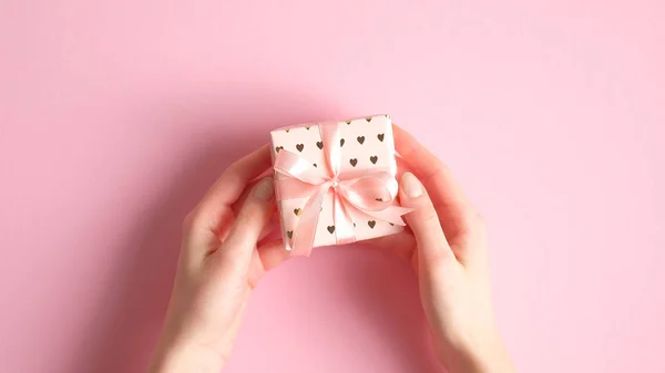 Cadeaudoosje in vrouwelijke handen over roze achtergrond. Flat lay minimalistische stijl, bovenaanzicht. Valentijnsdag, verjaardag, Moederdag aanwezig concept. — Stockfoto