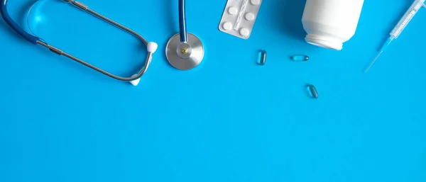 Medical banner design with pediatric doctor equipment on blue background. Top view table with stethoscope, pills and syringe. Healthcare and medical concept.