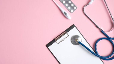 Pembe arka planda tıbbi ekipman ve aletler. Stetoskop, medikal pano, termometre ve haplar. Tıbbi afiş tasarım şablonu. Kopyalama alanı olan üst görünüm