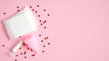 Regl hijyen ürünleri. Üst düzey hijyenik ped, tekrar kullanılabilir adet bardağı ve pembe arka planda konfetili tampon. Kritik günler, adet döngüsü, kadın sağlık konsepti