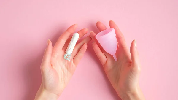 Manos femeninas sosteniendo tampón y copa menstrual sobre fondo rosa. Comparación de diferentes tipos de productos de higiene menstrual. Días críticos, ciclo menstrual, concepto de salud femenina —  Fotos de Stock