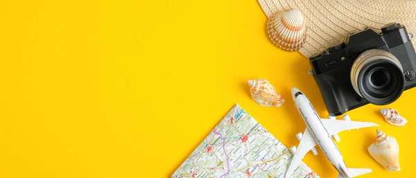 Travel banner design template with airplane model, map, vintage camera, beach hat and seashells on yellow background. Top view with copy space. Travel summer holiday vacation concept