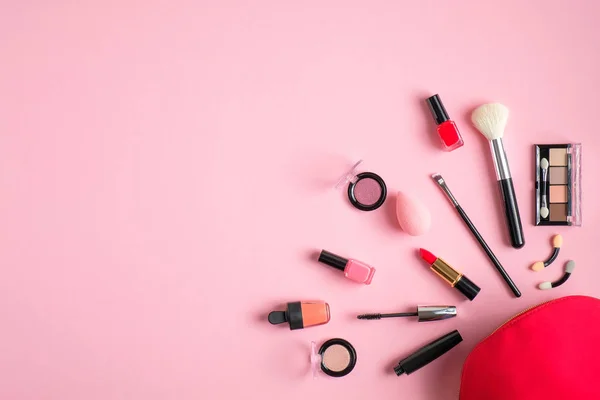 Красный макияж сумка с косметическими продуктами проливается на пастельно-розовый фон. Плоский, вид сверху — стоковое фото