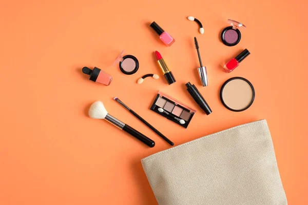 Cosmetics bag with makeup products spilling out on pastel peach background. Flat lay, top view