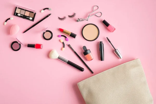 Cosmetics bag with makeup products spilling out on pastel pink background. Flat lay, top view