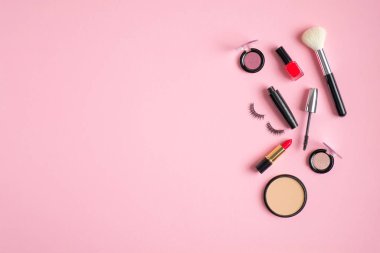 Makeup products and cosmetics spilling out on to pastel pink background. Flat lay, top view, copy space. Woman make-up concept.