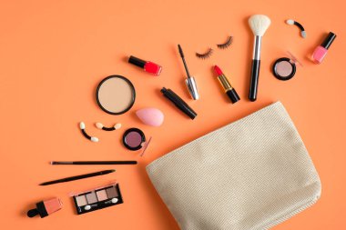 White makeup bag and cosmetic products spilling out on to pastel peach color background. Flat lay, top view. Stylish make up artist pouch with beauty products. Female make-up concept