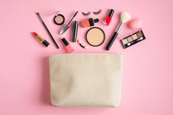 Makyaj çantası ve kozmetik ürünler pastel pembe arka plana dökülüyor. Düz yerde, üst tarafta. Cazibeli makyaj sanatçısı çantası ve profesyonel güzellik ürünleri