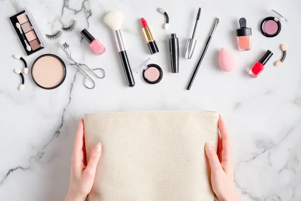 Borsa per il trucco su mani femminili e prodotti cosmetici di bellezza che si rovesciano sulla scrivania in marmo. Posa piatta, vista dall'alto. Bellezza e concetto di moda — Foto Stock