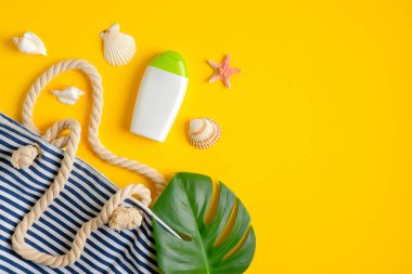 Güneş kremi şişesi, yeşil tropikal yapraklar, çizgili plaj çantası, sarı arka planda deniz kabukları. Güneş koruması, güneş kremi, kozmetik ürünler, yaz cilt bakımı. Düz yatış, üst görünüm