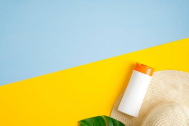 Güneş kremi şişeleri, yeşil tropikal yaprak, mavi ve sarı arka planda izole edilmiş kadın plaj şapkası. Güneş koruması, güneş kremi, cilt bakımı. Düz yatış, üst görünüm