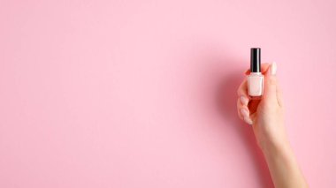 Pembe arka planda tırnak cilası şişesini tutan bir kadın. Manikür, pedikür, güzellik salonu konsepti.